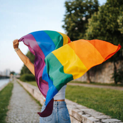 Young woman with rainbow LGBTQIA+ flag running on city quay