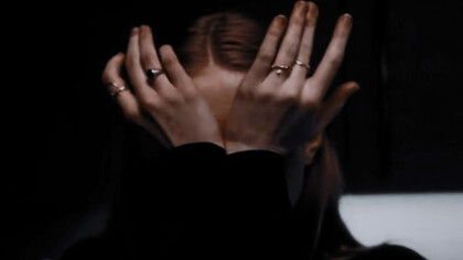 A woman, overwhelmed by emotion, conceals her tear-streaked face with her trembling hands