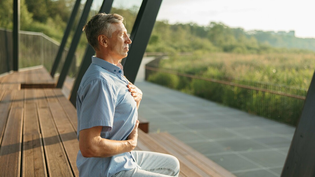 An older man resting one hand on his chest and the other on his abdomen as he breathes deeply, symbolizing awareness of the body's natural rhythm