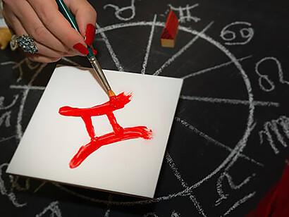 Female astrologer draws gemini zodiac sign on white tile