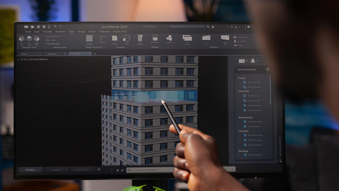An architect engineer analyzing a construction model on a computer, pointing at an architectural building prototype