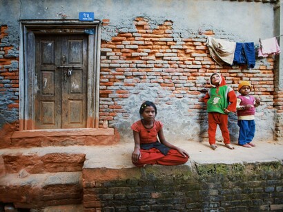 Children gathered outside a worn brick home, representing the human cost of persistent inequality despite global abundance