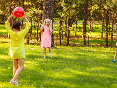 Summer day in the park, two little girls and boys playing with a red ball on the green grass