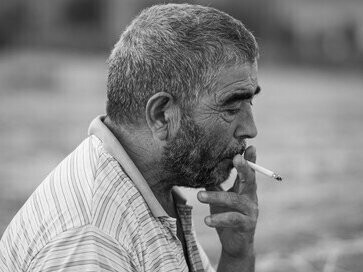 Idoso fuma enquanto observa o movimento da rua. Por muito tempo observei esse senhor aqui da janela, todo dia, por volta das quatro horas da tarde ele aparecia, ficava sentado na lombada que há em uma loja da esquina e ali permanecia por longo tempo fumando um cigarrinho, observando o movimento e, certamente, a mulherada, isso eu tenho certeza que ele fazia porque seus olhos e o movimento da cabeça quando elas passavam não deixavam a menor dúvida
