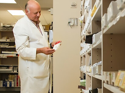 In the bustling pharmacy, a dedicated male pharmacist meticulously inspects a medication from the neatly organized inventory