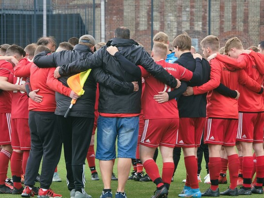 A soccer team stands in a circle with their coach, showing camaraderie, support, and team bonding before a match