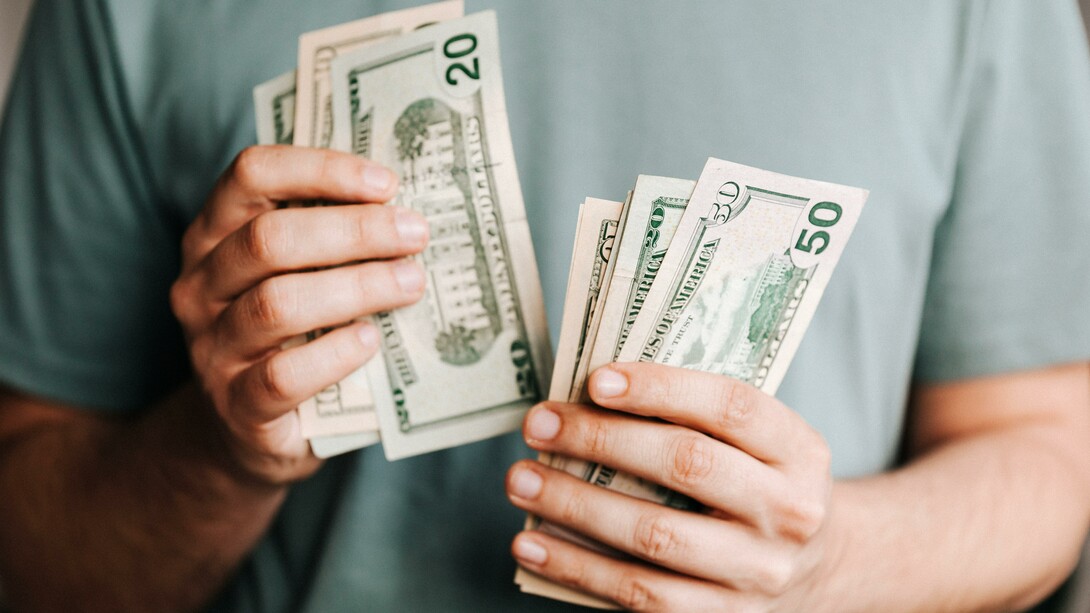 A person holding dollar banknotes. Investing is a realm where the principles of collaboration and shared growth contradict the notion of a zero-sum game