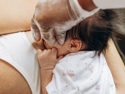 Mulher segura o bebê nos braços enquanto o amamenta em um momento de intimidade e cuidado. Para além da nutrição, o artigo destaca a diversidade de componentes presentes no leite materno e seu papel na saúde infantil
