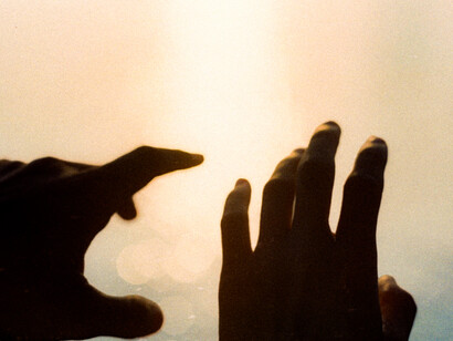 Dos manos se encuentran frente a una luz intensa, entre sombras y reflejos