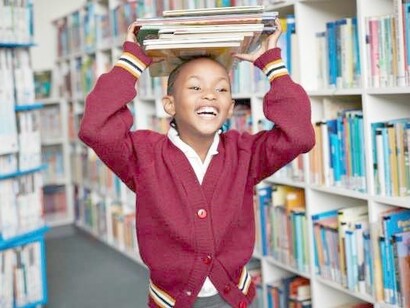 Happy South African child smiling and happy, with books on her head, in the school's library
