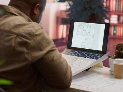 A computer screen displaying 3D rendering software showcasing an architectural building complex in a modern architect's office, with a man actively working on the digital twin project