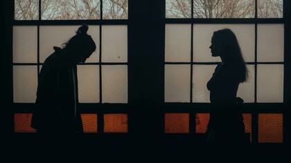 A man and woman standing in a dimly lit room, surrounded by darkness and emotional tension