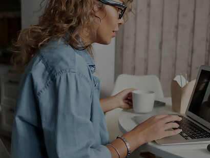 As the morning sun streams into the room, a woman sits by her computer, coffee in hand, engaged in a lively video chat with another woman. The connection transcends distance, creating a virtual space for shared conversations and moments of connection