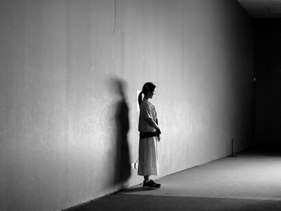 A dramatic black-and-white portrait of a solitary figure standing in a vast minimalist hallway, emphasizing isolation and the power of negative space
