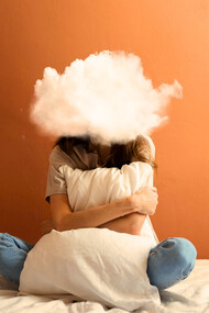 A woman sitting on her bed with a cloud in place of her head, representing the mental fog created by constant overthinking