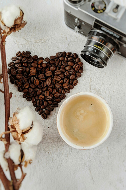 Coffee beans shaped into a heart, alongside a cup of coffee and a vintage camera