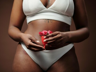 A soft and intimate image of a woman with a menstrual cup and red blossoms, reflecting the connection between menstrual health and bodily autonomy