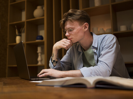 A young man studies in a virtual classroom and in a library, focusing on academic writing