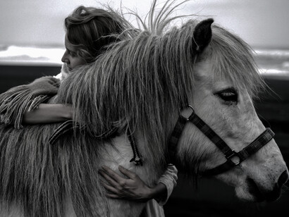 A woman stands on the beach and hugs her horse