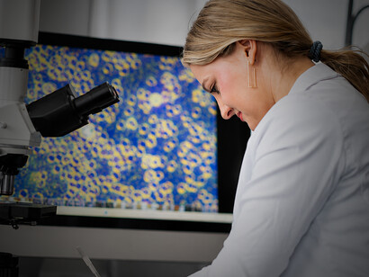 Woman scientist in a lab coat conducting biomedical engineering research using a microscope in a modern laboratory