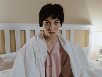 A woman sitting in bed, staring into the camera with sad eyes
