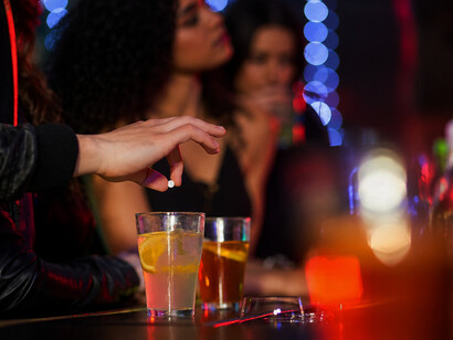 A man secretly slipping drugs into a drink at a bar, illustrating drug-facilitated sexual assault