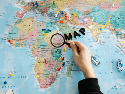 Un hombre revisa un mapa mundi con lupa. La pregunta que interesa en este contexto es el origen de los idiomas y las fuerzas que causaron su diversificación