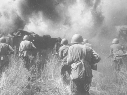 Soldiers slowly ease their way past the an exploding tank in Europe during WW2