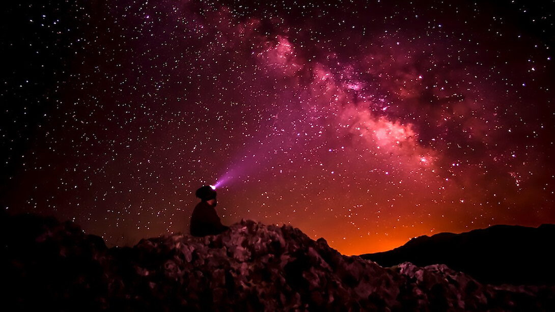 A striking silhouette photograph captures a person holding a flashlight against the backdrop of the Milky Way, evoking the enchanting beauty of the night sky