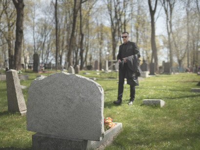 A man stands in a cemetery, grieving in silence as a funeral procession passes in the distance