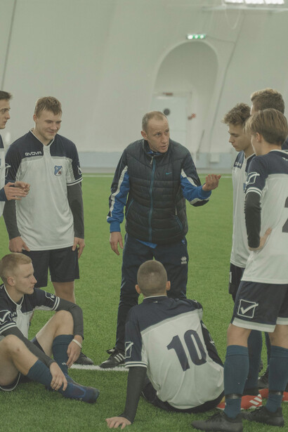 The coach guiding his team on the pitch, with the manager and sporting director discussing strategy