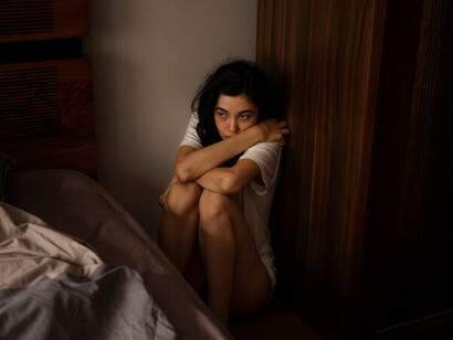 A young woman sitting on the floor next to her bed, struggling with anxiety