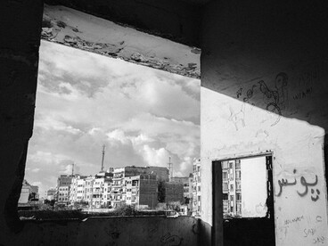 Perspectiva en blanco y negro desde una habitación derruida con pintadas y grafitis en las paredes, mirando hacia un paisaje urbano destruido por la guerra