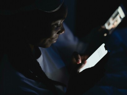 At night, a woman uses her phone in a dimly lit room surrounded by screens