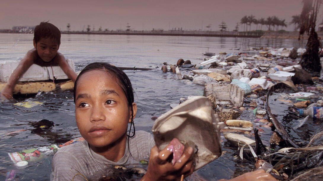Una niña sacando trozos de plástico de un río contaminado