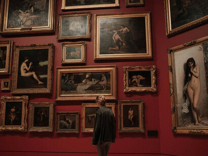 A woman walking through a gallery with historical paintings on dark red walls, illuminated by low light, showcasing art gallery illumination and exhibition space lighting
