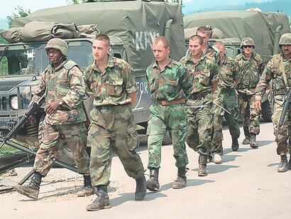 Corporal Clyde Bass and Sergeant Edsen Hughes from the U.S. Marine Corps' 26th MEU escort Yugoslav detainees to the Kosovar-Serbian border as part of NATO's Operation Joint Guardian, ensuring peace and stability in Kosovo