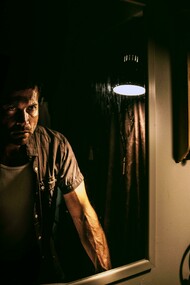 Man gazing into a mirror, gripping his face in confusion