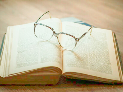 Glasses resting on an open book. We have to organize our knowledge into a definite plan of action and directing it to a definite end