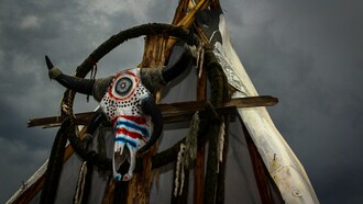 A ceremonial bull skull fixed upon a rustic wooden frame beneath a turbulent sky in Mexico, reflecting the lingering presence of ancestral belief systems