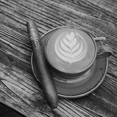 A perfectly crafted latte and a Cuban cigar rest on a weathered wooden table, blending two luxuries that demand time and appreciation