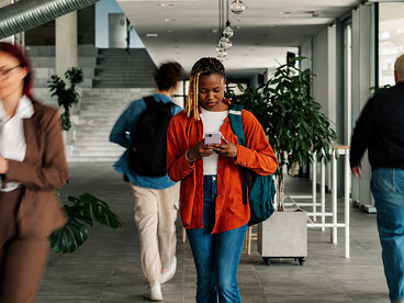 Engrossed in her phone, a young woman walks through a busy office corridor, detached from the dynamic environment surrounding her
