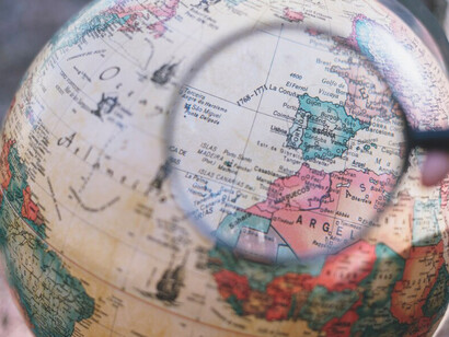 A person examining a globe with a magnifying glass, symbolizing a detailed exploration of global issues and geographical insights
