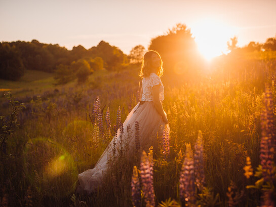 A woman in a bright dress walks across a field in the glow of sunset