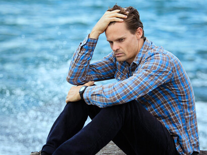 A sad man by the shoreline, symbolising the heaviness of despair and unanswered question