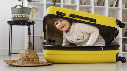 Smiling toddler sitting playfully inside an open suitcase