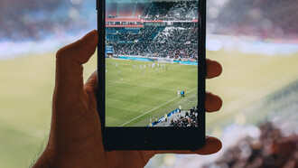 Persona mirando un partido de fútbol a través de su teléfono móvil