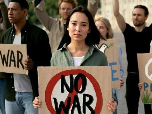 A demonstrator holding a cardboard anti-war sign, embodying civilian resistance to the escalation of global tensions