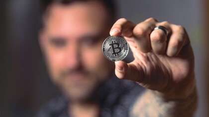 Pessoa segurando uma moeda Bitcoin prateada