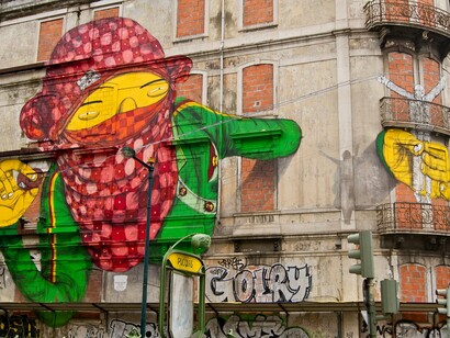 Obra sem título, mas reconhecida pelo nome "I love vandalismo", de Os Gêmeos, realizada em 2010 na Avenida Fontes Pereira de Melo, em Lisboa, Portugal. O plano aberto revela a intervenção em sua escala monumental, com o personagem encapuzado de vermelho ocupando a fachada e outras figuras integradas às janelas e à arquitetura do edifício. Criada para o Projeto CRONO, a obra exemplifica a expansão internacional da linguagem de Os Gêmeos e sua capacidade de transformar o espaço público em território de expressão artística.